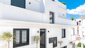 A modern two-story building with a white exterior, black shutters, and potted plants. - Stunning Apartment in Cómpeta (Cómpeta)