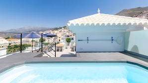 A rooftop pool with a view of a mountainous town, a white building with a tiled roof, and a blue umbrella. - Stunning Apartment in Cómpeta (Cómpeta)