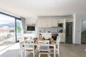 A modern kitchen with white cabinets, a stainless steel refrigerator, and a dining area with white chairs and a wooden table.