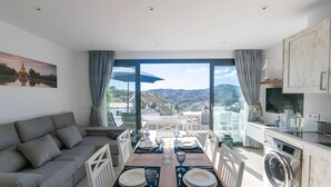 A modern living room with a sofa, dining table set for four, and a view of mountains. - Stunning Apartment in Cómpeta (Cómpeta)