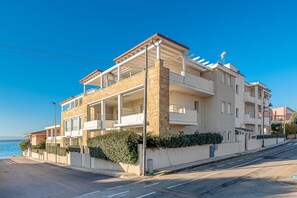 Un edificio de varios pisos con balcones, fachada de piedra y vista al mar.