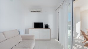 Un saló modern amb un sofà, una televisió de pantalla plana, un forn microones i una porta corredissa de vidre que condueix a una zona exterior.