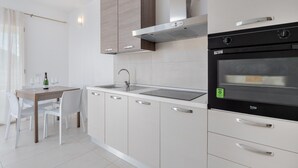 Una cuina moderna amb forn integrat, taula de dinar amb caires i finestra amb cortines lleugeres.
