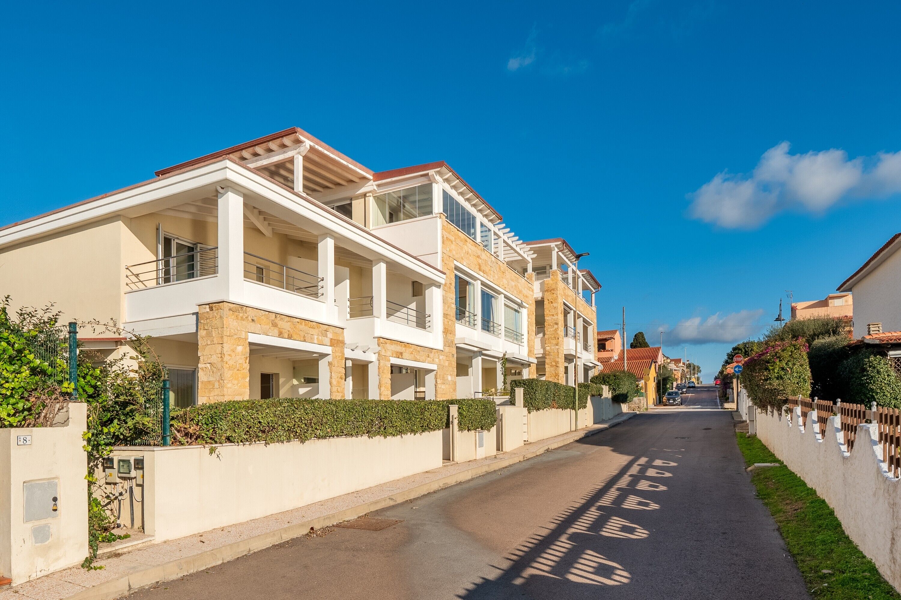 Una calle residencial con casas modernas de dos pisos, cielo despejado y una acera bien conservada.