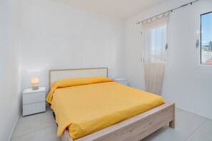 Un dormitorio con cama, mesita de noche, lámpara y ventana con cortinas.