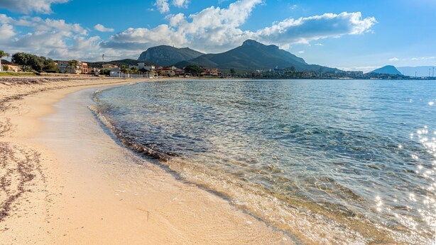 Una playa con agua cristalina, una orilla arenosa y montañas a lo lejos.
