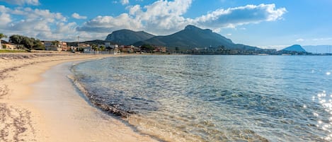 Una playa con agua cristalina, una orilla arenosa y montañas a lo lejos.