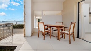Un espacio moderno para comer al aire libre con vista al mar, un pilar de piedra y una barandilla metálica.