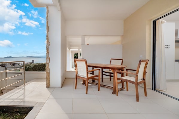 A modern outdoor dining area with a view of the sea, a stone pillar, and a metal railing.