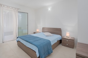 A bedroom with a bed, bedside tables, a nightstand, a curtain, and a sliding glass door.