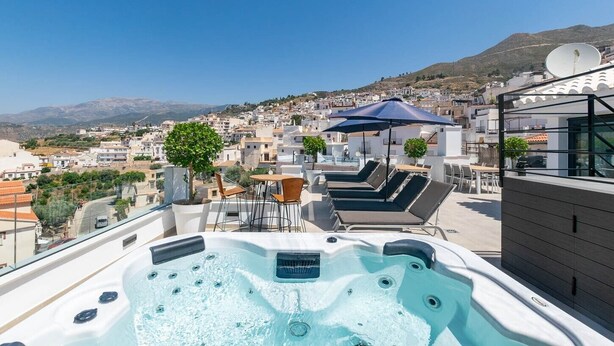 Eine Dachterrasse mit Whirlpool, Liegestühlen und Blick auf eine Hügelstadt.