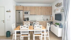 Eine moderne Küche mit Holzausbau, einer eingebauten Mikrowelle und einem Essbereich mit weißen Stühlen und einem Holztisch.