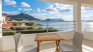 A balcony with a view of the sea, a wooden table, and two chairs.