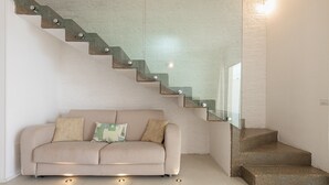 A modern interior with a beige sofa, a glass staircase, and a white wall.