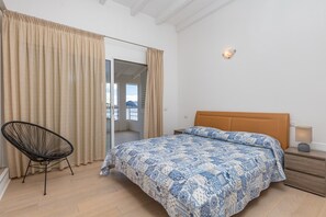 Une chambre à coucher avec un lit, une chaise, une table de chevet et une vue sur l’extérieur, visible à travers une porte.