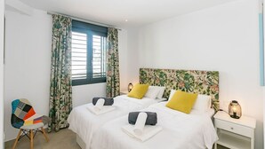 A bedroom with two beds, floral curtains, a colorful chair, and a nightstand with a lamp. - Luxury Apartment with shared swimming pool and jacuzi (Cómpeta)