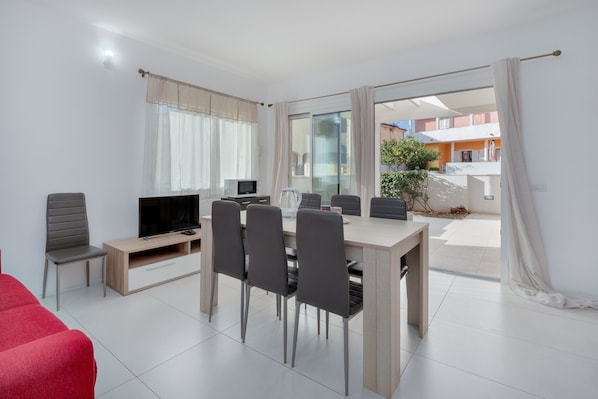 Una sala de estar moderna con televisor, mesa de comedor, sillas y un sofá rojo.