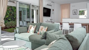 A modern living room with a sofa, a flat-screen TV, and a dining area with chairs. - Villa "Cormorani 1" with Sea View, Jacuzzi & Wi-Fi (golfo aranci)