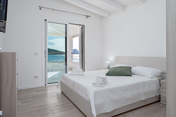 Una camera da letto con un letto, un comodino, una lampada, un cuscino verde, una finestra vista mare e una porta scorrevole in vetro.
