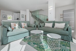 A modern living room with a green sofa set, two white round coffee tables, and a staircase with glass railings. - Villa "Cormorani 1" with Sea View, Jacuzzi & Wi-Fi (golfo aranci)
