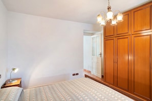 Une chambre à coucher avec un lit, une table de chevet, une lampe, une armoire et un lustre.