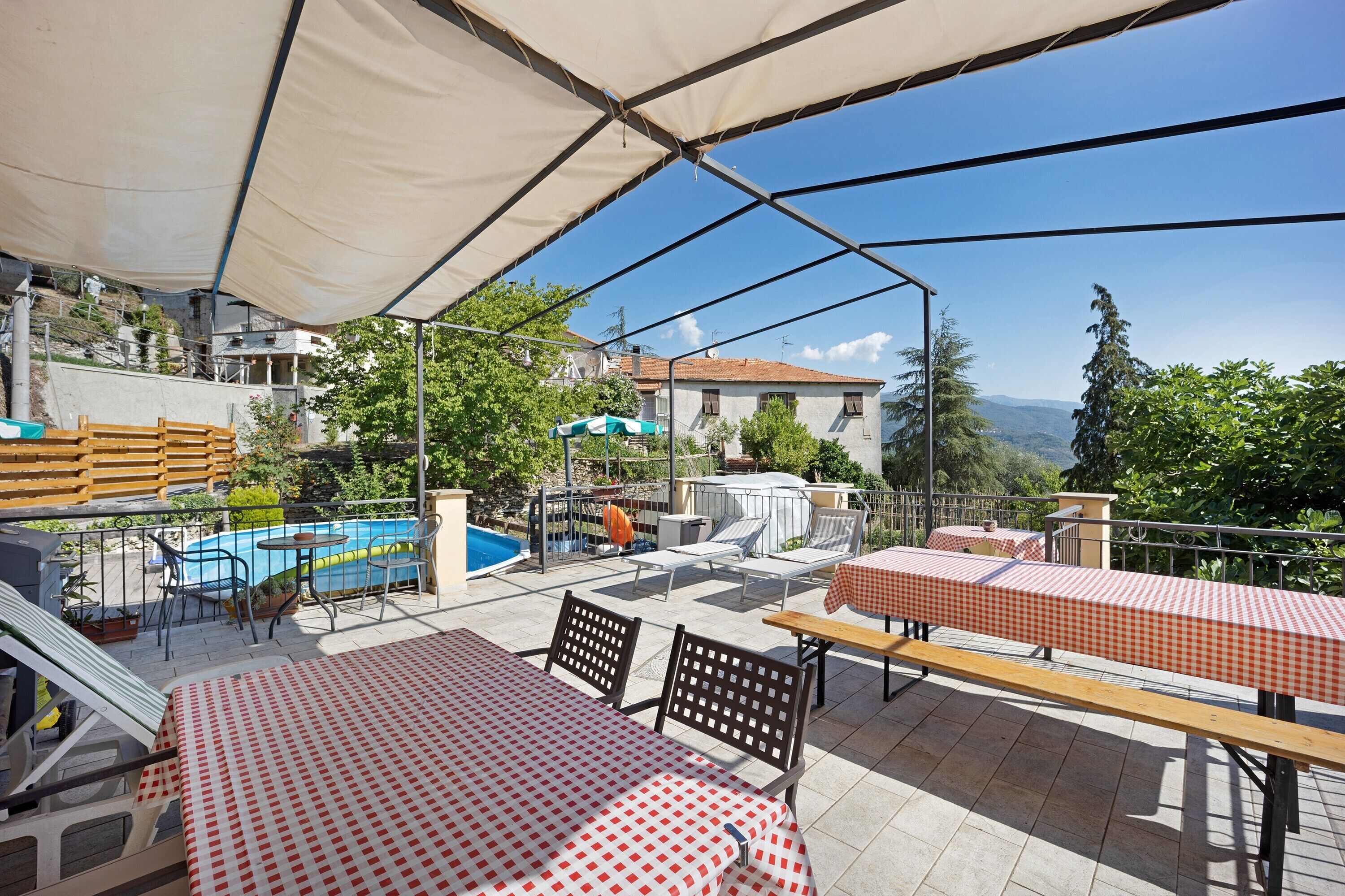 An outdoor patio with tables and chairs, a pool, and a view of the surrounding landscape.