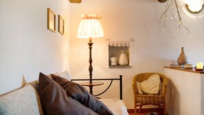 Ein Schlafzimmer mit einem Bett, einem Sessel, einer Lampe und einem kleinen Regal mit Gegenständen.