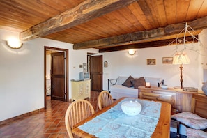 Un comedor con una mesa de madera, sillas y un camino de mesa decorativo. Se observa un sofá y una lámpara al fondo.