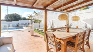 A covered patio with a wooden table and chairs, a pool, and a white wall with a decorative fence. - Villa 'Jardin Tropical' with Private Pool, Garden A/C & Wi-Fi (Manilva)