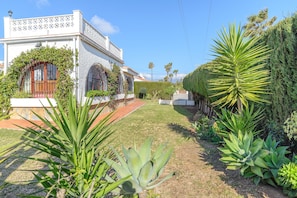 Un bâtiment blanc avec un jardin, un chemin pavé et un palmier.