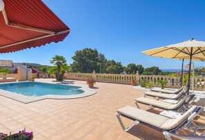 Ein Poolbereich mit Liegestühlen und Sonnenschirm, umgeben von einer gefliesten Terrasse und einem dekorativen Zaun.