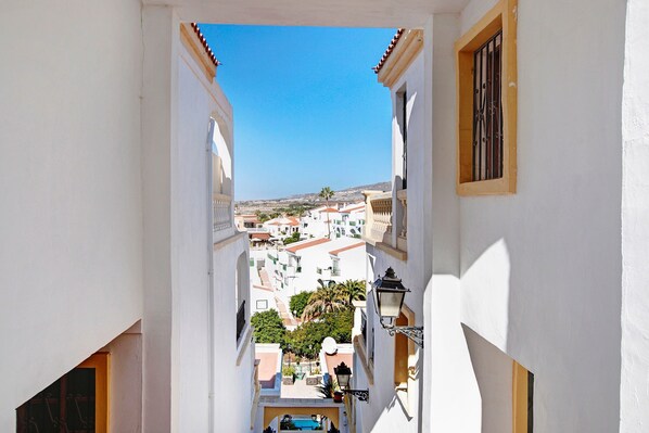 Une rue étroite bordée de bâtiments blancs, un ciel d’un bleu limpide et une vue sur la ville en contrebas.