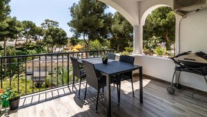 Un balcón con mesa y sillas, una parrilla y vistas a árboles y edificios.