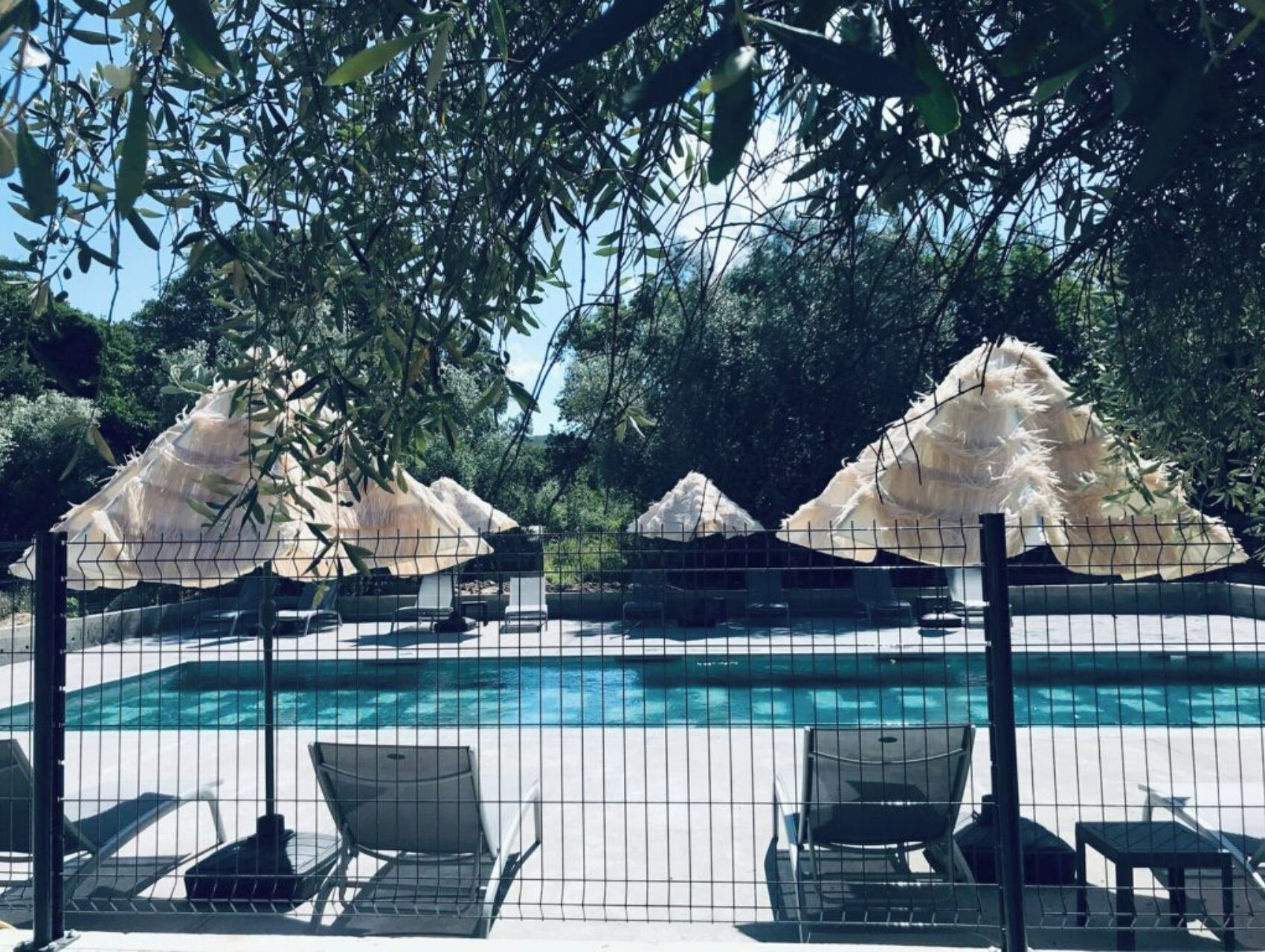 Un área de piscina con sillones de descanso y sombrillas de paja.