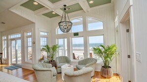 Una habitación con un gran ventanal con vista a la playa, un candelabro y un rincón de estar con dos sillones y una mesita de centro.