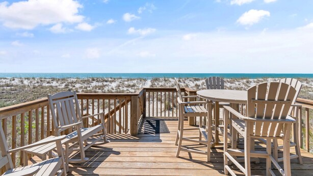 A wooden deck with chairs and a table overlooking a beach. - Oceanfront 4BR, 2BA house on Oak Island, sleeps 10—perfect for family getaways! (Oak Island)