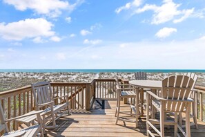 A wooden deck with chairs and a table overlooking a beach. - Oceanfront 4BR, 2BA house on Oak Island, sleeps 10—perfect for family getaways! (Oak Island)