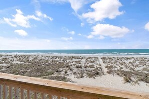 A beach with a wooden railing, sandy dunes, and the ocean.