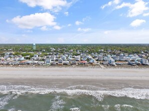 A coastal residential area with houses along the beach, a water tower, and a clear sky.