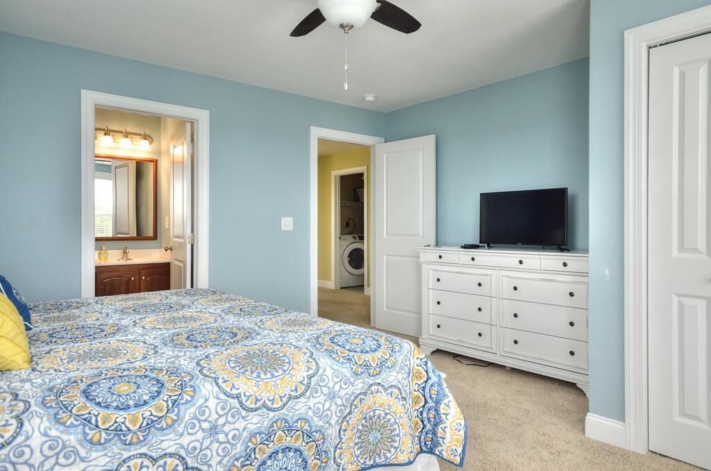 Un dormitorio con cama, cómoda, televisor y ventilador de techo.