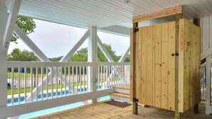 Ein überdachter Außenbereich mit Holzterrasse, weißer Geländer und Blick auf ein Schwimmbecken.