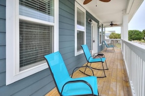 A covered porch with blue chairs and a wooden floor.