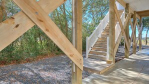 Eine Holztreppe führt zu einem überdachten Bereich mit Kiesweg und Bäumen im Hintergrund.