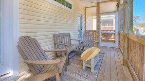 Eine überdachte Veranda mit Adirondack-Stühlen, einer Holzbank, Holzwertlauf und Deckenventilator.