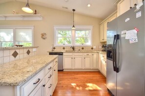 A kitchen with white cabinets, granite countertops, a stainless steel refrigerator, and a window with a view of trees.
