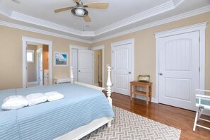 A bedroom with a bed, a ceiling fan, a wooden floor, and white doors.
