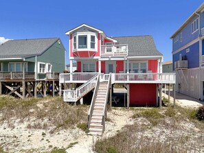 Una casa sulla spiaggia con una veranda in legno, una scala che conduce a un balcone e una combinazione di colori rosso e bianco.