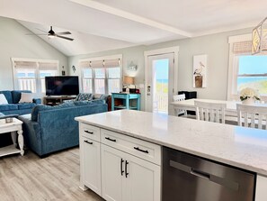 A modern living room with a sofa, TV, and dining area. - Oceanfront retreat, Sea-ing Starrs in Oak Island, offers 5 bedrooms for 10 guests. (Oak Island)