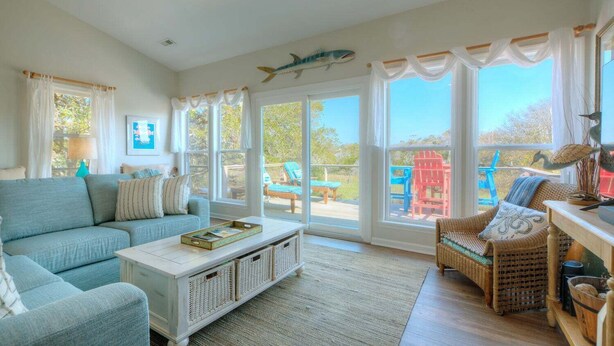 Ein geräumiges Wohnzimmer mit einer Couch, einem Couchtisch, Korbstühlen und Blick ins Freie.