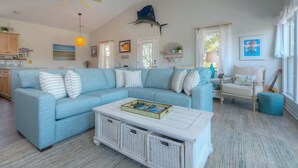 Ein Wohnzimmer mit einem hellblauen Sofa, einem weißen Couchtisch, einem Deckenventilator und einem Wandbild in Fischform.